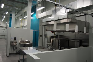 commercial kitchen with hood vent, hand washing sinks, food sink, stainless steel tables.