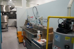 three compartment sink with containers of cleaning chemicals connected by tubes for use